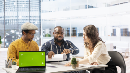 Clients negotiating with the realtor next to isolated copy space on laptop, examining layout and blueprints for a new high class office space. Business people investing in property with financier.