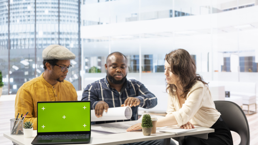 Clients negotiating with the realtor next to isolated copy space on laptop, examining layout and blueprints for a new high class office space. Business people investing in property with financier.